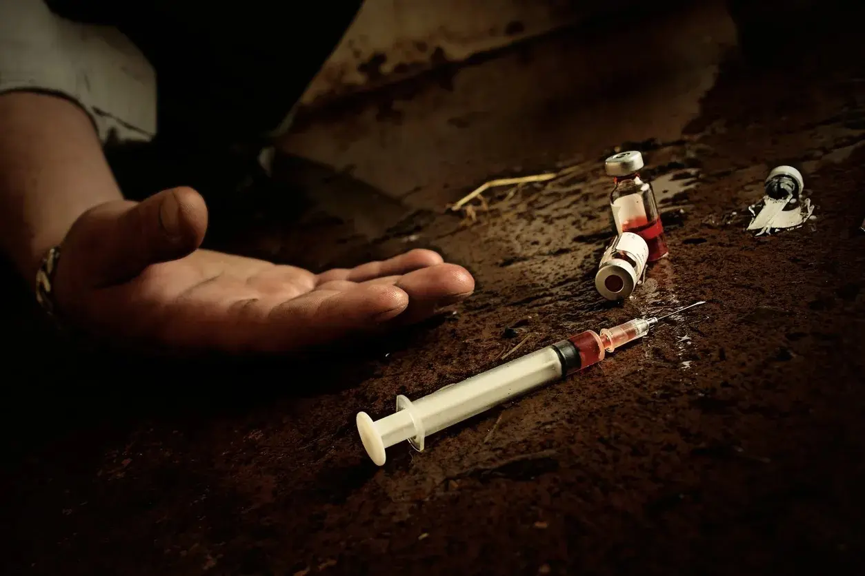 Person's hand beside scattered syringes